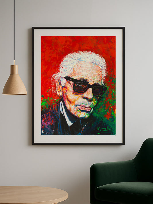 Framed 75×100 cm Karl Lagerfeld fine art print by Marcel Kozik displayed in a modern living room with minimalist decor, wooden pendant lamp, and green velvet chair.